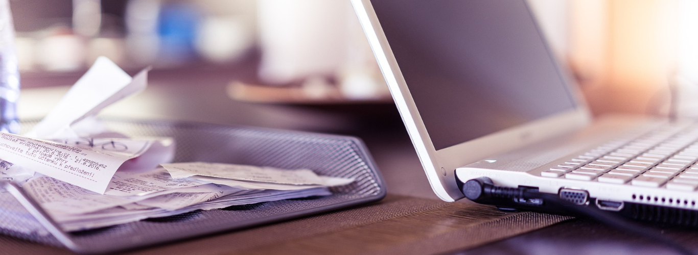 a laptop computer sitting on a desk with a stack of papers